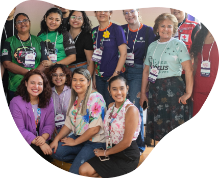 Grupo de cerca de doze mulheres sorridentes posando para foto. Algumas estão em pé e outras agachadas à frente. A maioria usa crachás de evento e camisetas de projetos sociais e instituições.